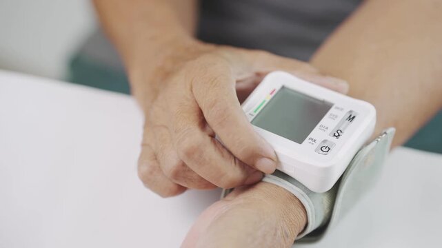 Close up of a senior pressing the start button on a digital wrist blood pressure monitor, representing home blood pressure monitoring, hypertension management, preventive healthcare, selfcare.
