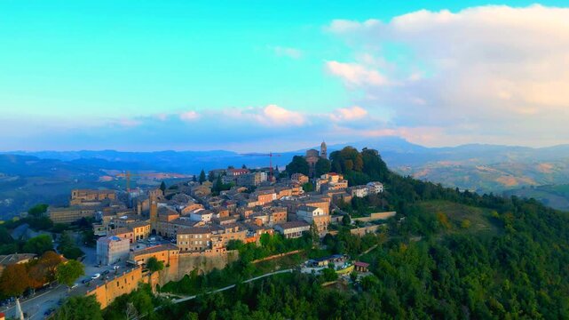 Interesting aerial push-in tilt-down shot in Santa Vittoria in Matenano, the tightly-knit town centre surrounded by rich vegetation, perched on a sumptuous, lofty hill, between ravines, hills, clouds