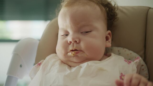 Young baby exploring new flavors, experiencing messy eating while wearing a bib during a mealtime in a high chair