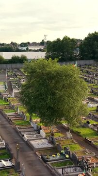 Travelling 60FPS vertical social ratio aerial video of Milltown Cemetary and the Republican Plot in West Belfast, Northern Ireland in the UK on a bright sunny day. Produced with Rec709 colour.