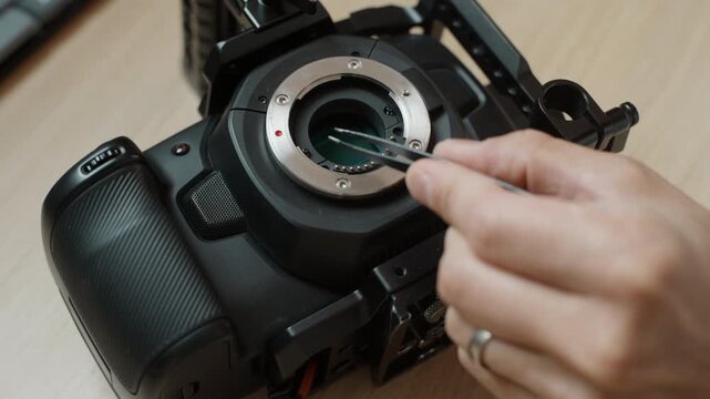 shot of tweezers removing two small screws from the lens mount of a cinema camera, the sensor exposed, to access and remove the IR cut filter. A detailed look at camera modification and sensor work