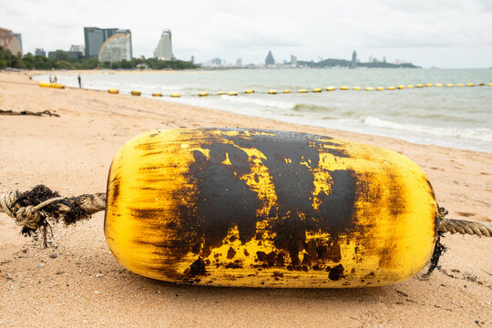 Buoy and rope covered in crude oil residue washed up on sandy beach, marine oil spill pollution and environmental disaster concept