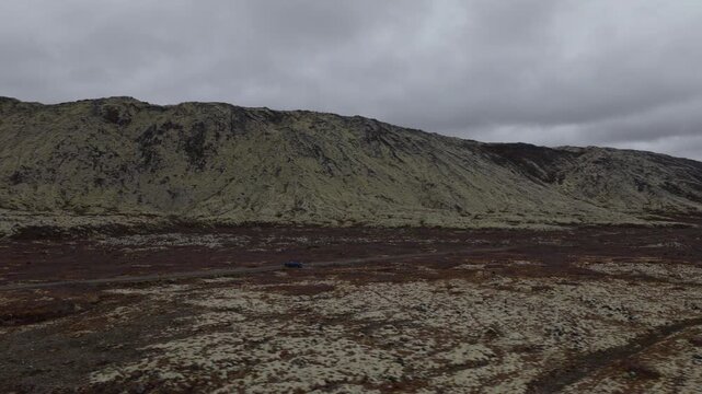 Volcanic ridge rises above barren mineral terrain at Seltun in the Krysuvik area of Reykjanes, Iceland, with sparse vegetation covering the rugged ground, aerial orbit.