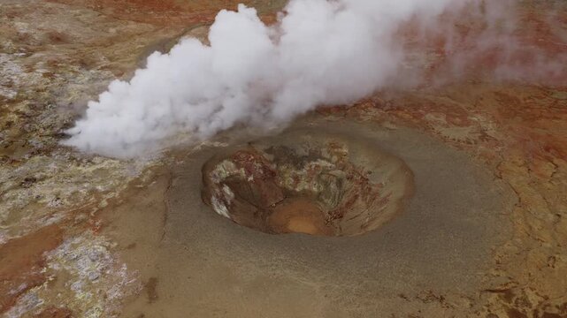 Seltun geothermal mud pool emits dense steam from a mineral crater in Krysuvik, Reykjanes Peninsula, Iceland, surrounded by rust-colored volcanic ground, overhead descent.