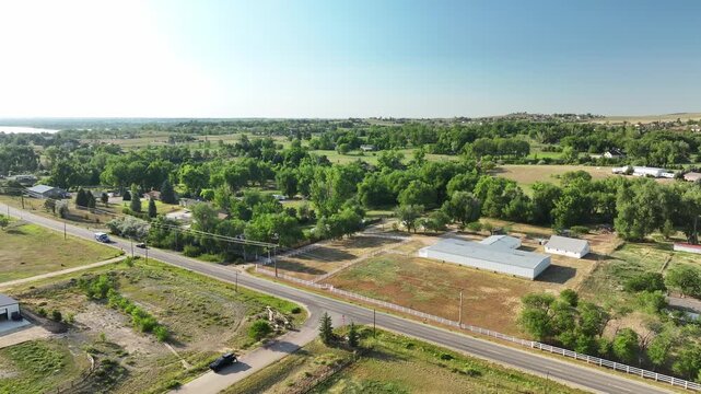 Sunny afternoon overhead view of country homes and expansive farm plots bordering West First Street in Colorado.
