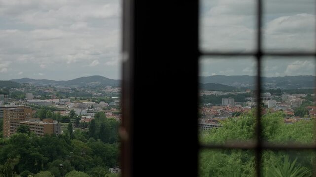 Guimar&atilde;es city view through open wooden window with green hills and red rooftops