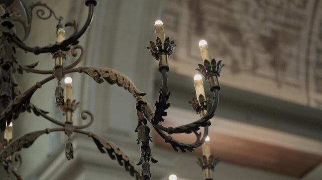 Ornate wrought iron chandelier arms with electric candle bulbs in grand interior