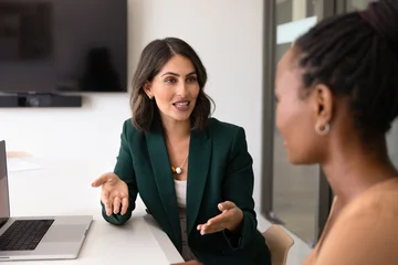 Fotobehang Sportwinkel Professional Latina woman conducts negotiation with female client sit at office desk with laptop in office, provide information about company services, make business proposal explain contract details  © fizkes