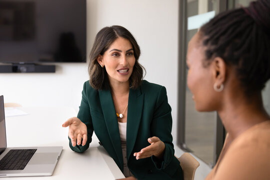 Professional Latina woman conducts negotiation with female client sit at office desk with laptop in office, provide information about company services, make business proposal explain contract details
