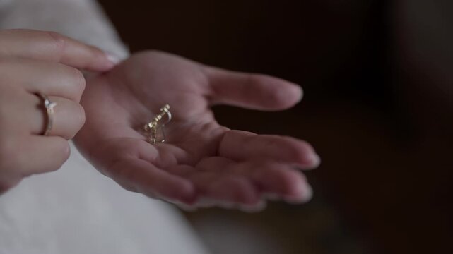 Bride holding delicate gold earrings in open palm with engagement ring visible