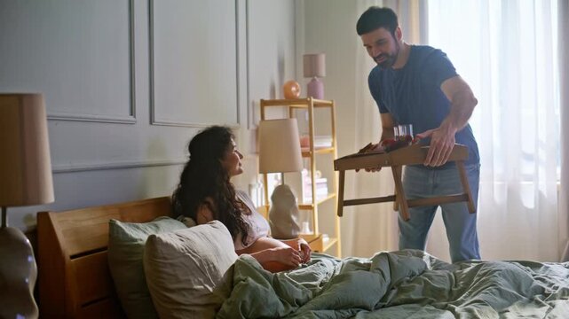 Man serving breakfast tray pregnant wife bed. Loving couple morning cuddle home.
