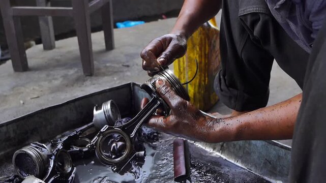 Mechanic cleaning engine piston parts in a workshop, automotive repair and maintenance service.