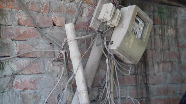 Old electric meter and tangled wires on a rustic brick wall in a rural village setting.