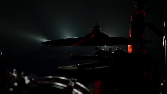 Silhouette of drum kit and cymbal on a dark concert stage with dramatic backlight. Atmospheric live music scene with percussion equipment ready for performance.