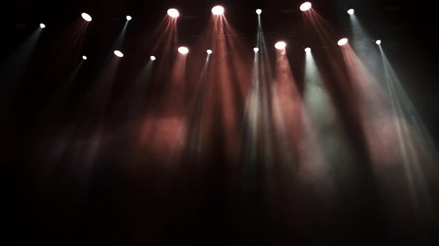 Professional stage lights turn on as spotlight beams move and focus through haze during lighting setup and testing before a live event.