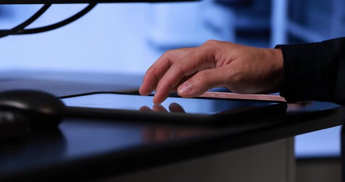 Close-up of a hand tapping a tablet screen on a desk in a modern workspace