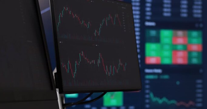 Multiple computer monitors display complex financial data. Glowing screens showcase vibrant red and green candlestick charts, perfectly illustrating live market trends