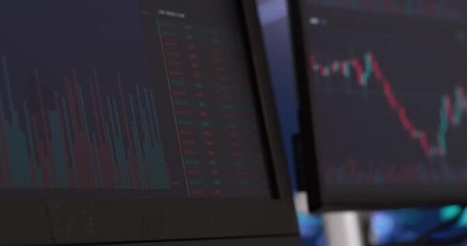 Multiple computer monitors display complex financial data. Glowing screens showcase vibrant red and green candlestick charts, perfectly illustrating live market trends