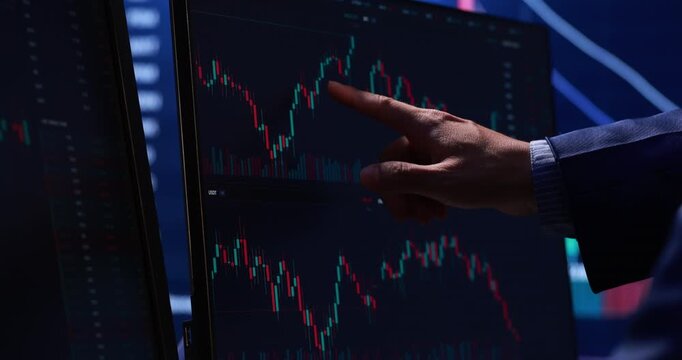 Hand pointing at a stock market chart on a computer screen in a dark office