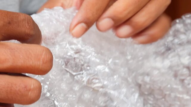 Man&rsquo;s hands squeezing and popping plastic bubble wrap at home for stress relief.