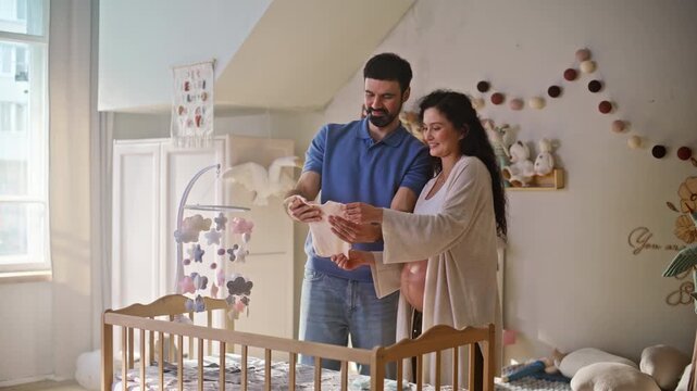 Couple holding baby bodysuit nursery. Man touching pregnant belly at home.