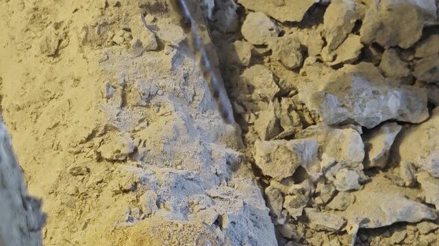 a heavy-duty rotary hammer drill bit drilling into a concrete structure. Plumes of white dust particles and stone chips spray upward as the tool chisels through mortar and concrete rubble