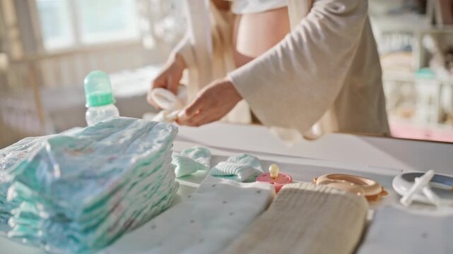 Expectant mother preparing pacifier bottle changing table. Closeup belly caress