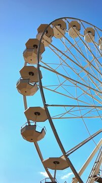 Low angle view of large ferris wheel slowly rotating against bright blue sky during sunny day.
