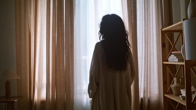 Expectant mother cradling belly window light. Backlit pregnancy silhouette home.