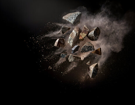 Exploding stone fragments with dust cloud on black background, shattered rock pieces flying in mid-air, dynamic mineral debris explosion with brown earth particles