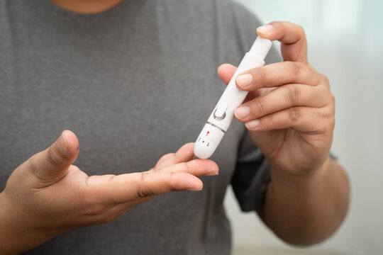 Asian woman self testing to check blood sugar level diabetes by digital lancet on finger at home.