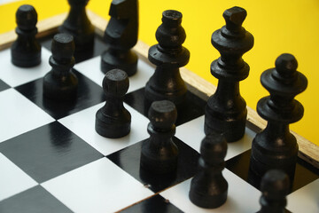 Black wooden chess pieces lined up on checkered chessboard with vibrant yellow background, strategic thinking, leadership, planning, and competitive game concept. © Nungkysoer