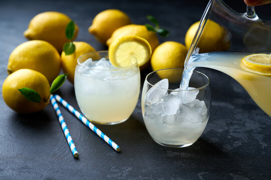 Lemonade with fresh lemon in glasses on dark background. Cold refreshing lemonade for summer party and fun.