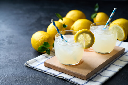 Lemonade with fresh lemon in glasses on dark background. Cold refreshing lemonade for summer party and fun.