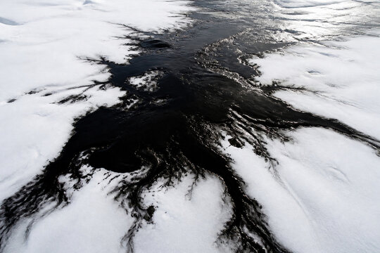 A vast white snowfield defiled by a sprawling black oil spill, aerial view.