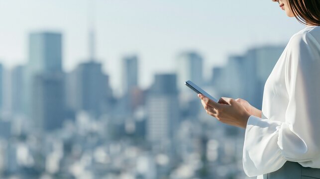 暮れゆく大都市を背景に窓際でスマートフォンを操作する女性