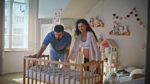 Expecting parents preparing baby crib nursery. Husband embracing pregnant wife.