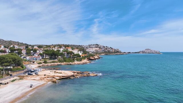 Aerial cruises alongside the classic Mediterranean Coast of Cala del Moro over clear waters, beaches, and rocky shore, towards the Peniscola old town. Spain.