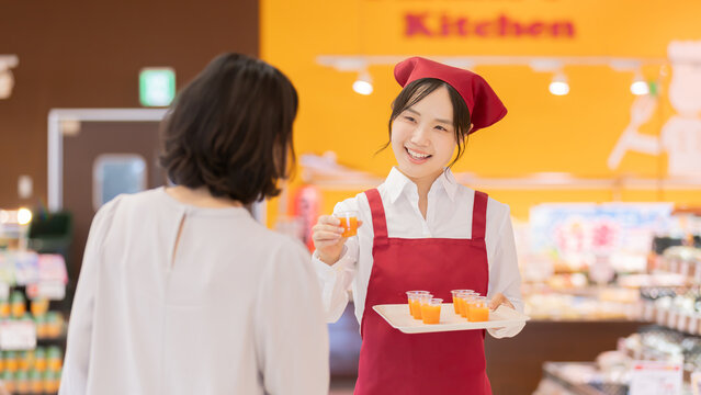 スーパーマーケットで女性客に試飲ドリンクを勧める笑顔の女性スタッフ