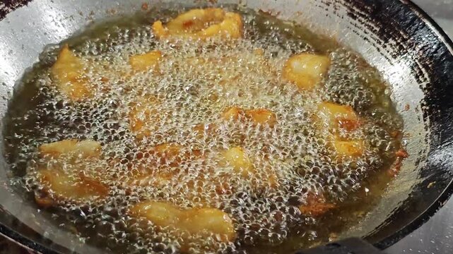 Battered fish pieces deep frying in a wok of boiling oil.