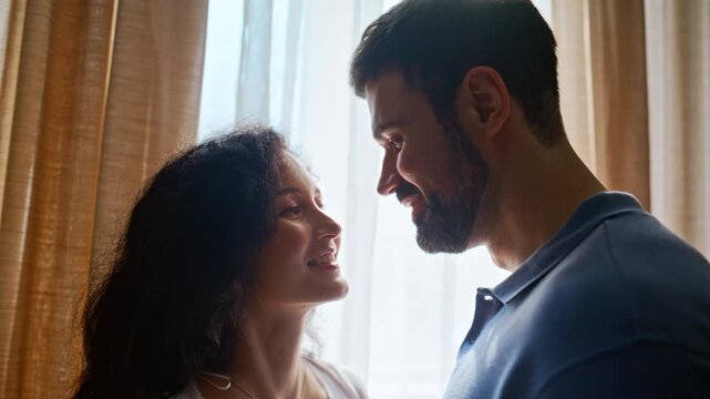 Expecting couple bonding window light. Man touching pregnant belly home moment.