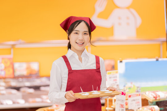 スーパーマーケットで試食をおすすめする笑顔の女性スタッフ
