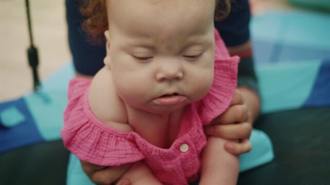 Baby with Down syndrome getting physical therapy, a parent supporting her during development exercises for special needs