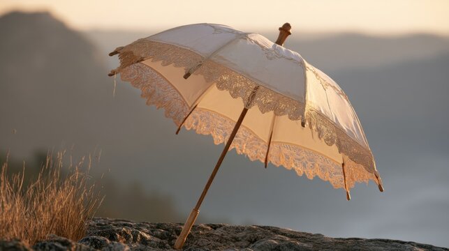 Elegant vintage parasol with lace detailing resting on a rocky surface during sunset with a breathtaking background of mountains and golden skies