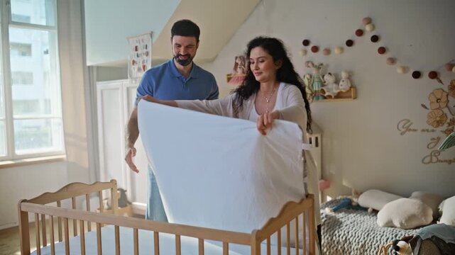 Pregnant wife husband preparing baby crib nursery. Couple making cot home.