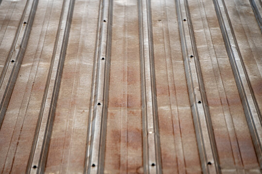 Old, weathered corrugated metal sheeting featuring patches of rust and clearly visible vertical ridges. Galvanized iron or zinc roofing or wall panels.