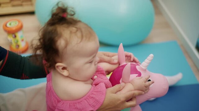 Little baby girl doing physical therapy exercises with a parent or therapist, developing motor skills with a toy