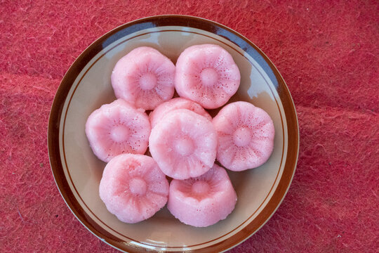 Plate of pink traditional Indonesian steamed cakes most likely kue apem or kue mangkok shaped like a flower or a bowl, with a slightly concave center.