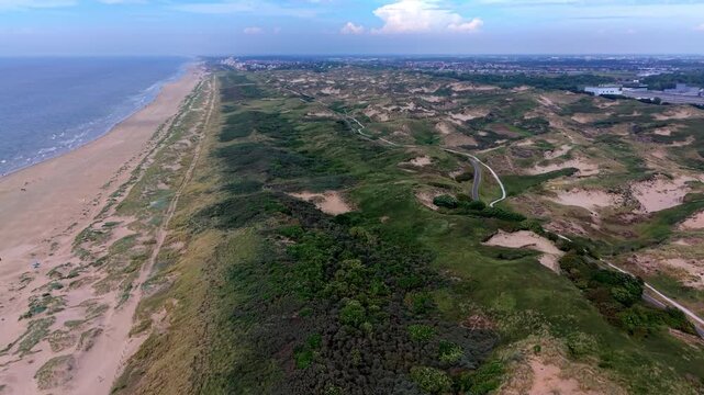 High angle horizontal aerial drone video clip of cycling path, walking trails, sand dunes, North Sea coast, and distant Scheveningen skyline in Meijendel, Wassenaar, South Holland, Netherlands