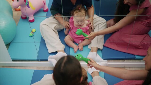 Baby sitting on a mat during early intervention physical therapy, playing with a toy and developing motor skills